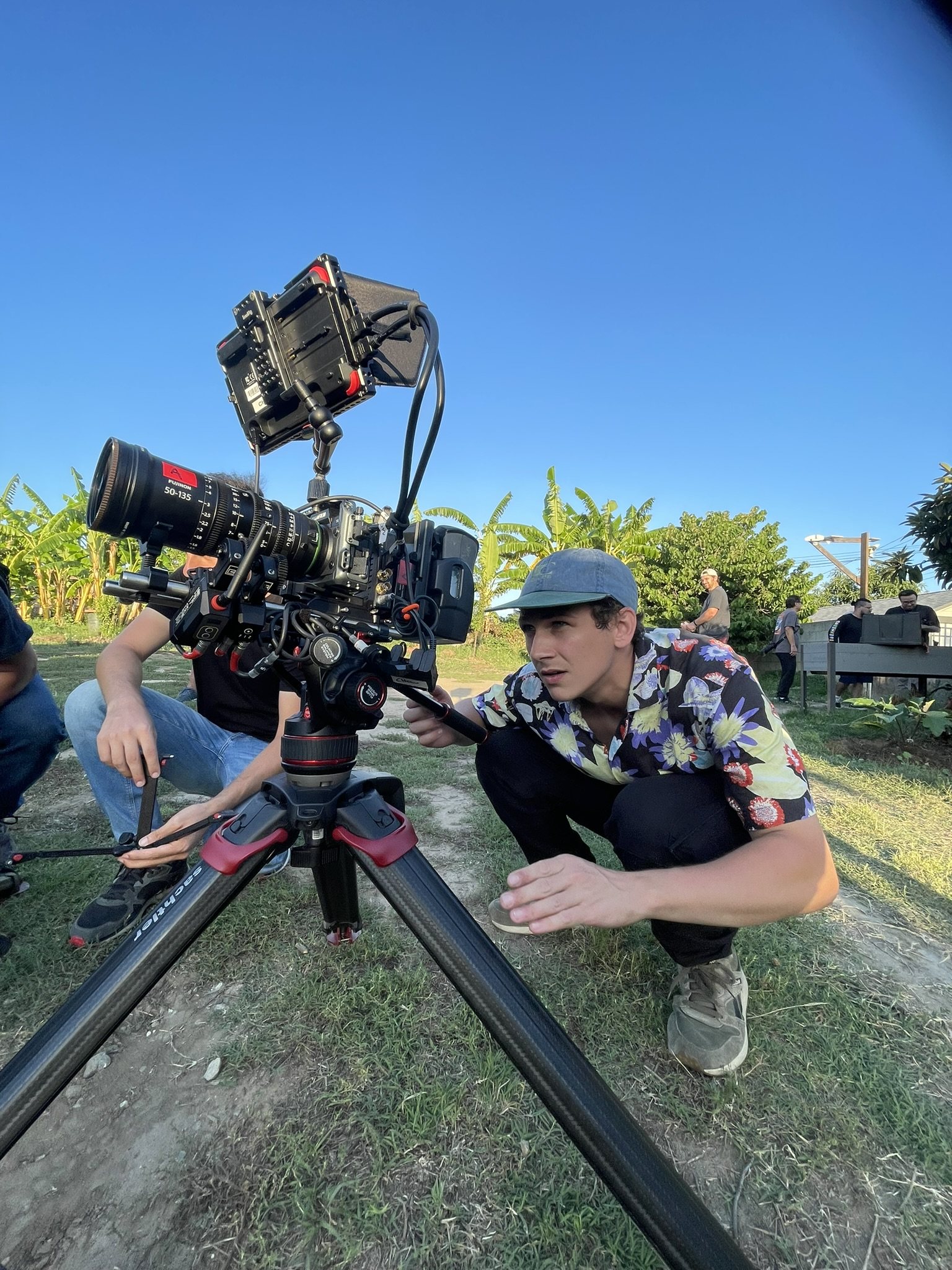 Eric adjusts a cinema camera mounted on a tripod outdoors.