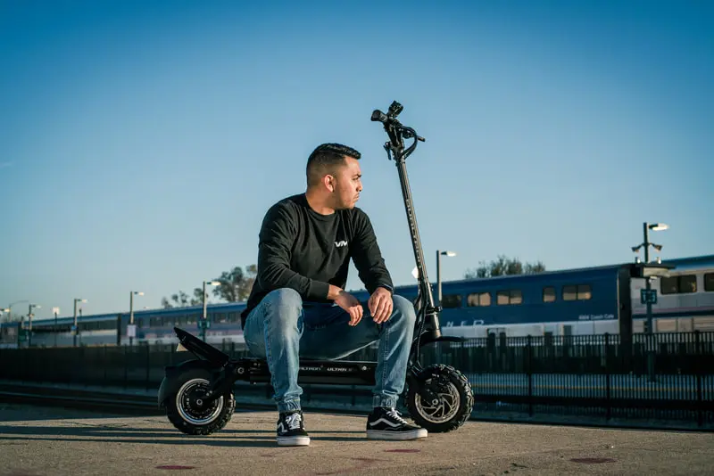 Rider and electric scooter photographed beside rail lines.