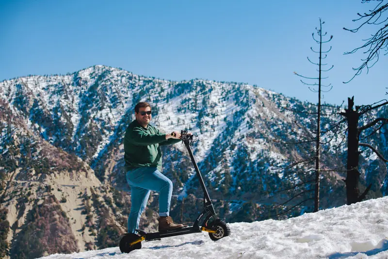 Rider with an electric scooter in a snowy mountain landscape.