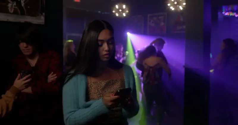 Two women stand together in a club washed with violet light.